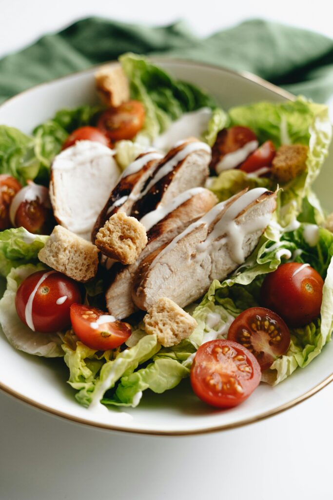 Delicious Caesar salad with grilled chicken, cherry tomatoes, and croutons in a white bowl.