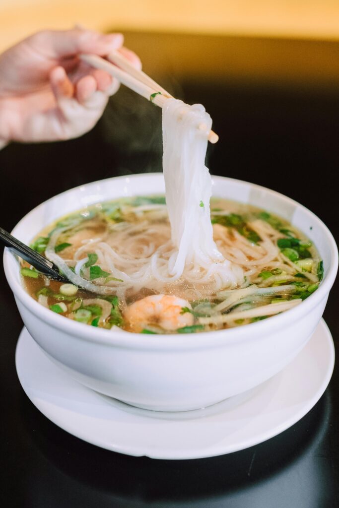 A steaming bowl of traditional Asian noodle soup with shrimp and greens, captured in elegant food photography.